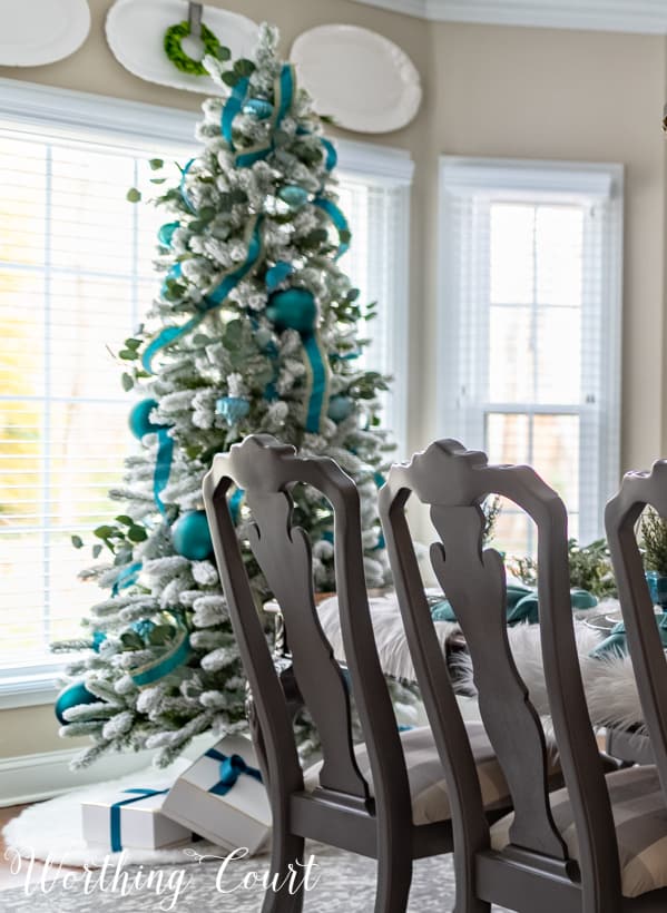 Flocked Christmas tree with teal decor and wrapped presents under the tree.