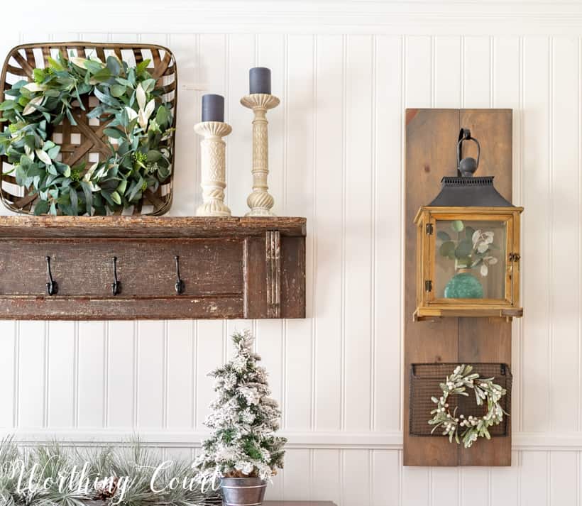 A basket on the wooden shelf that has a eucalyptus wreath inside it.