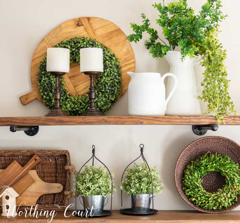 A wreath, candlesticks, a white pitcher filled with greenery.