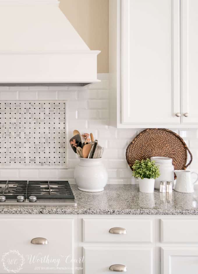 White kitchen cabinets with wicker tray leaning against the backsplash.