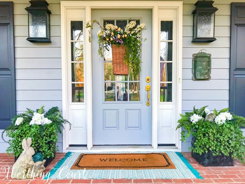 gray front door with sidelights flanked by planters and layered door mats