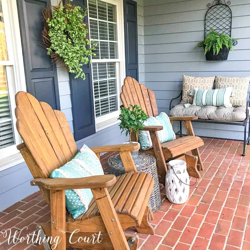 pair of wood stained adirondack chairs on a front porch with gray siding