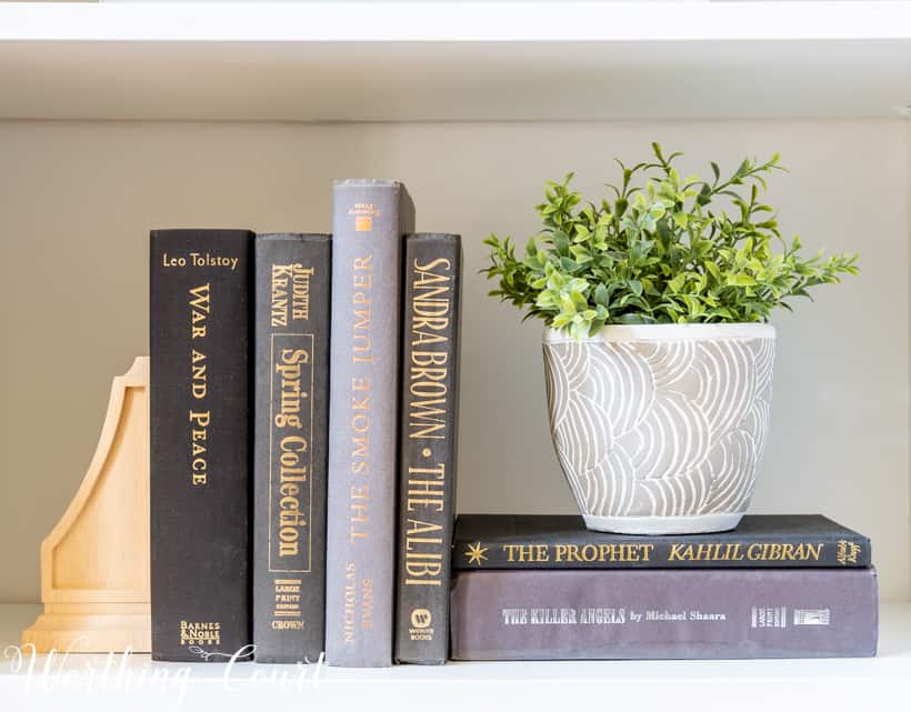 Bookshelf vignette with faux greenery and stacked books.