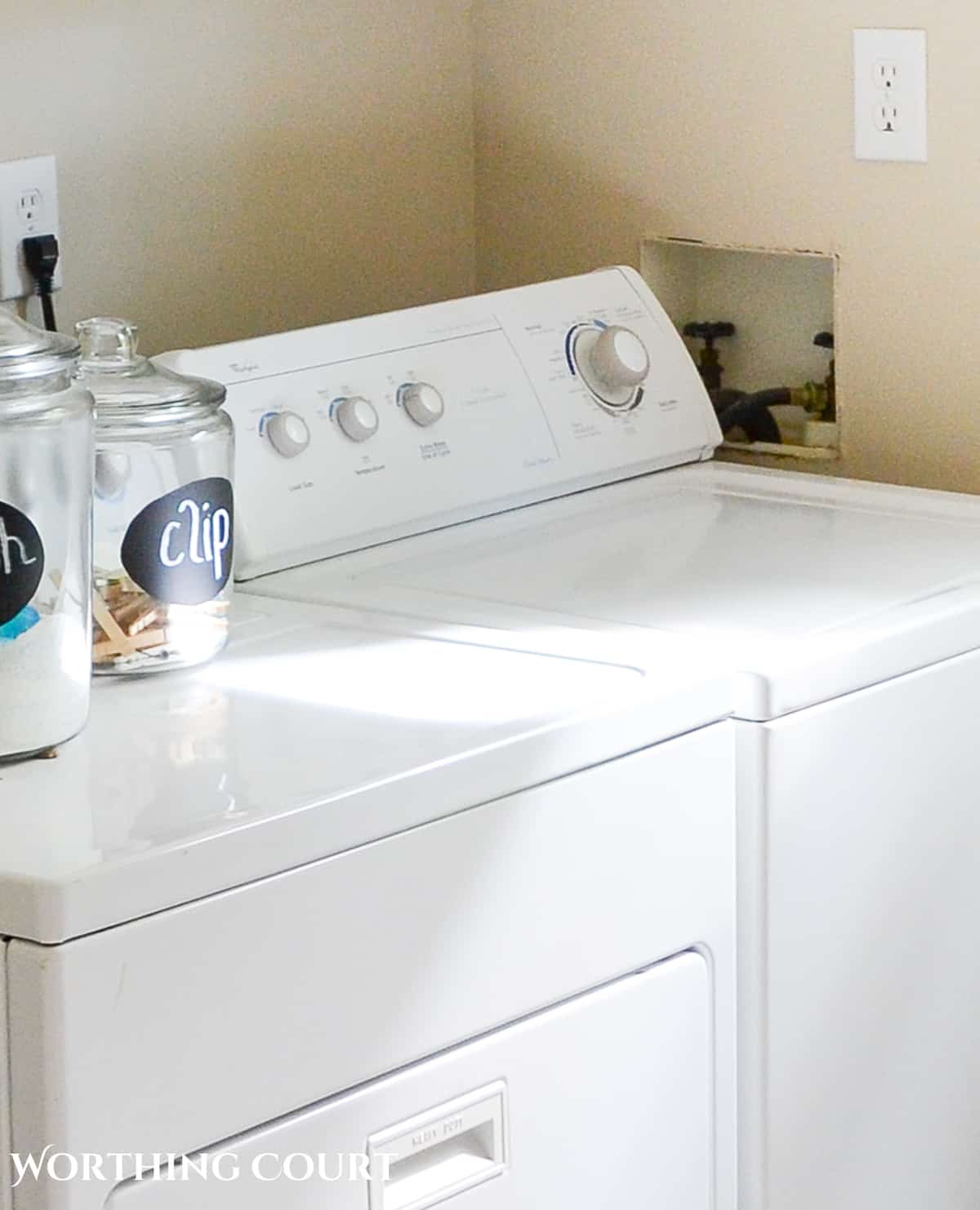 white washing machine beside hole in the wall for the washer hookups