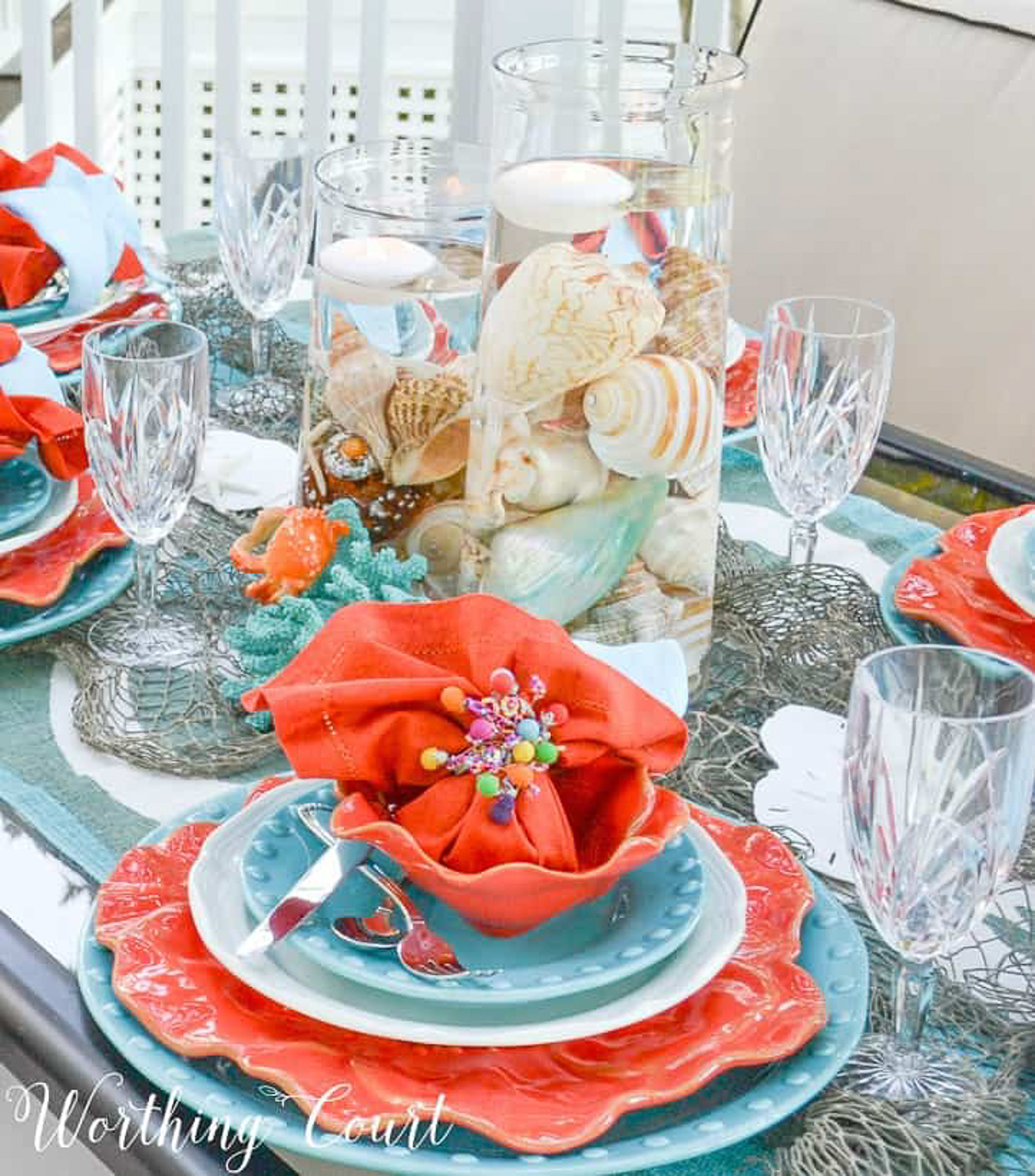 outdoor dining table set with a coastal theme using blue and coral dishware and coastal accessories