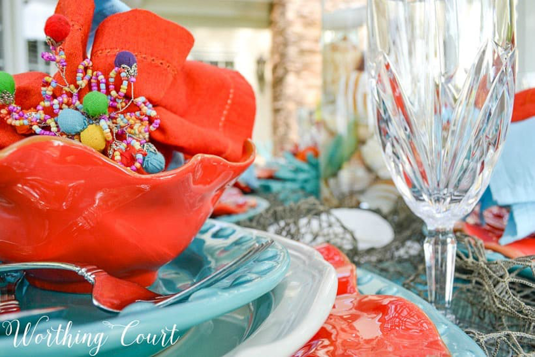 outdoor dining table set with a coastal theme using blue and coral dishware and coastal accessories