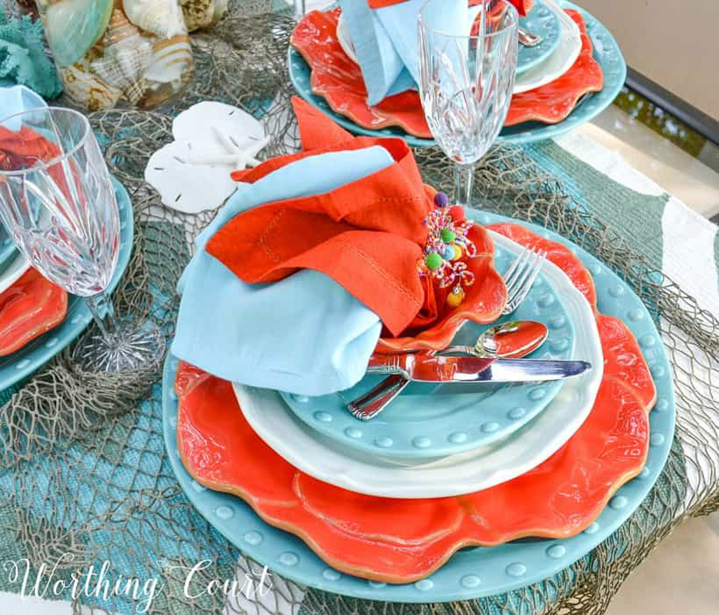 outdoor dining table set with a coastal theme using blue and coral dishware and coastal accessories