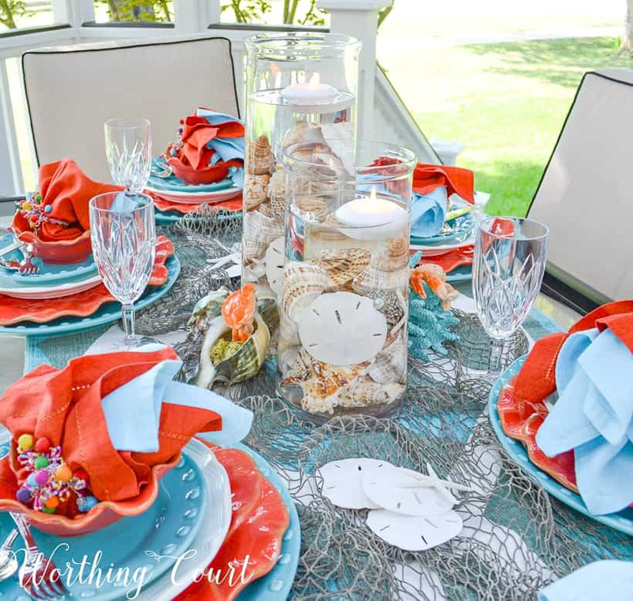 outdoor dining table set with a coastal theme using blue and coral dishware and coastal accessories