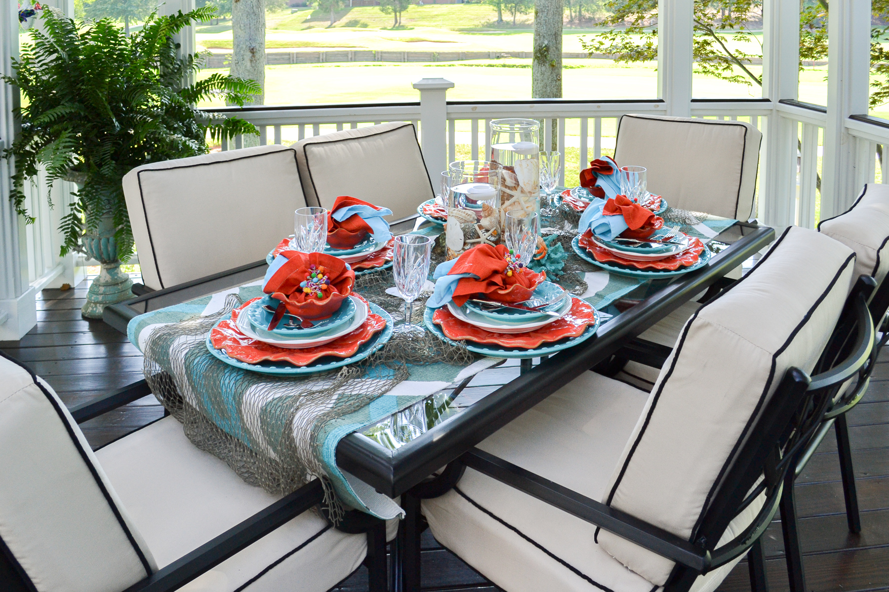 outdoor dining table set with a coastal theme using blue and coral dishware and coastal accessories