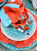 outdoor dining table set with a coastal theme using blue and coral dishware and coastal accessories