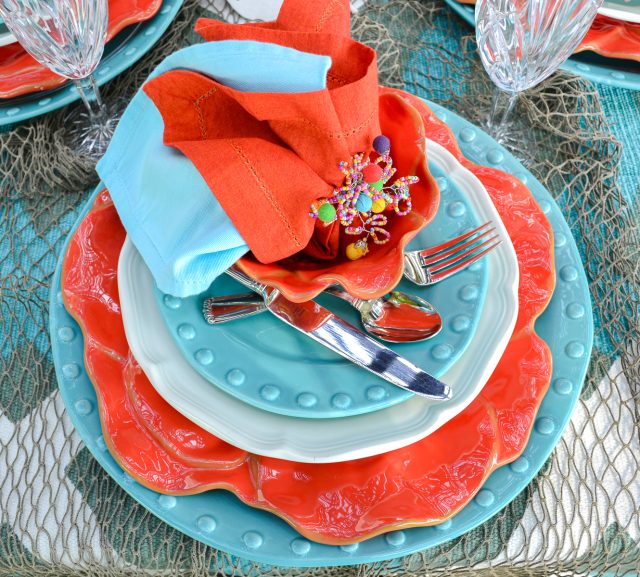 outdoor dining table set with a coastal theme using blue and coral dishware and coastal accessories