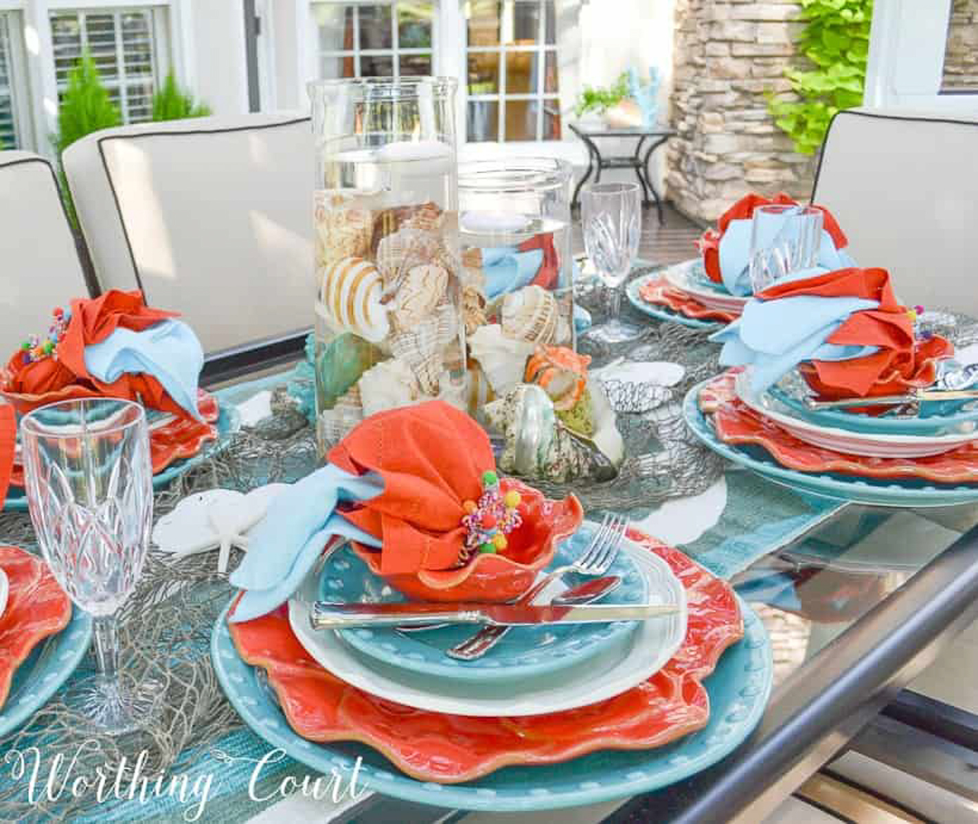 outdoor dining table set with a coastal theme using blue and coral dishware and coastal accessories