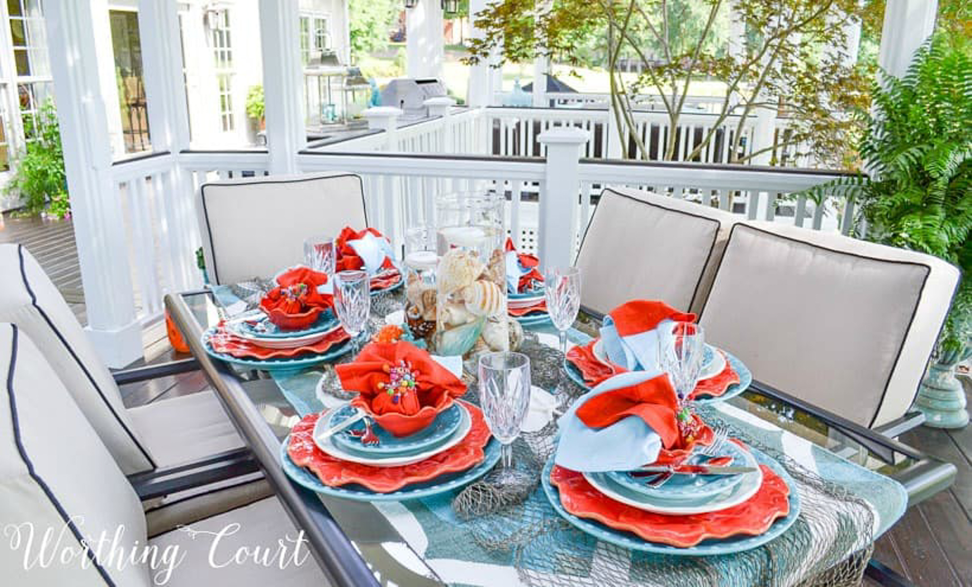 outdoor dining table set with a coastal theme using blue and coral dishware and coastal accessories