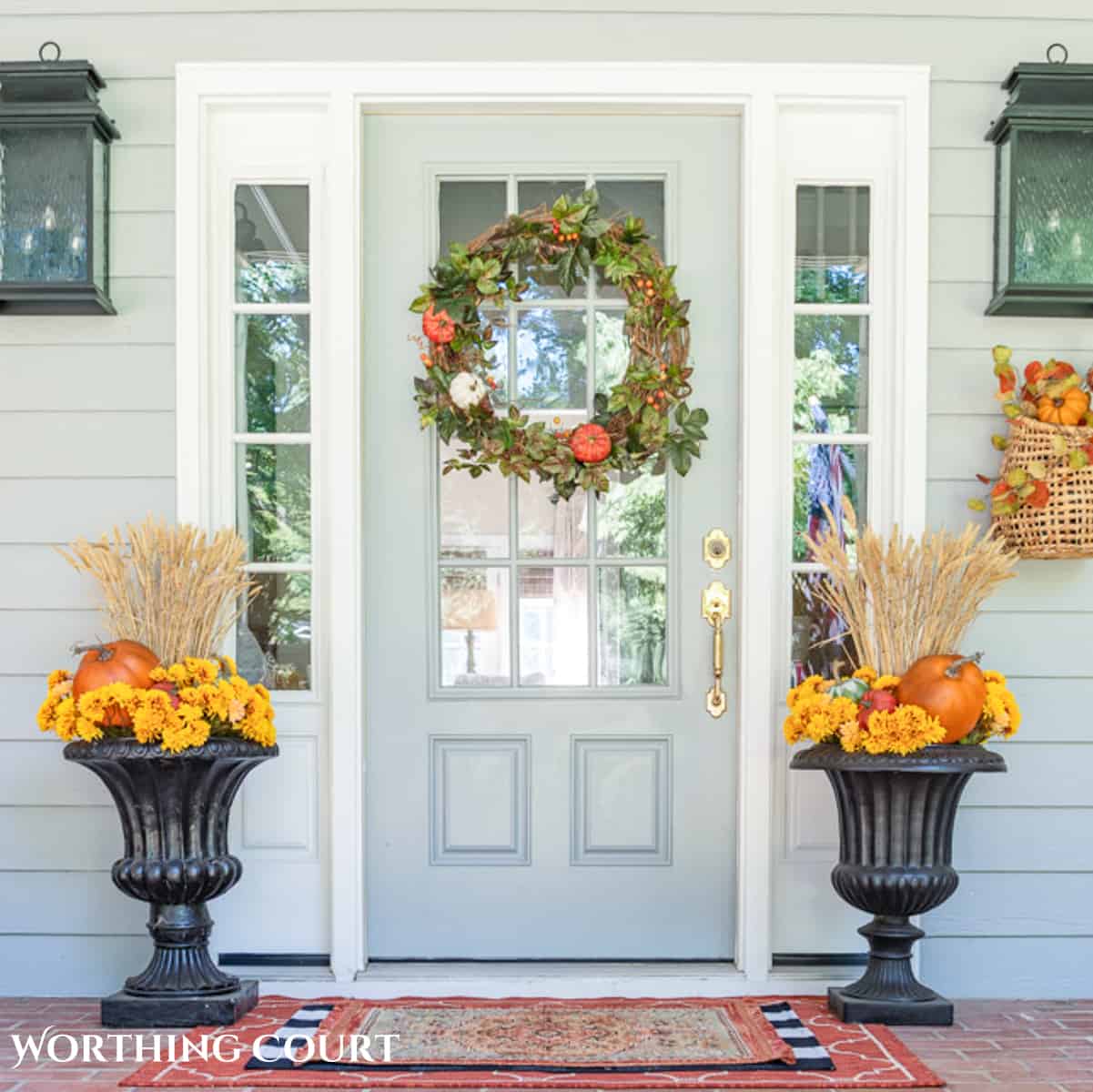 diy fall grapevine wreah on a gray front door flanked by urns filled with pumpkins and fall foliage