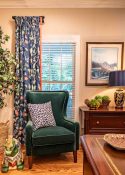 green velvet chair positioned in front of window with navy blue floral draperies