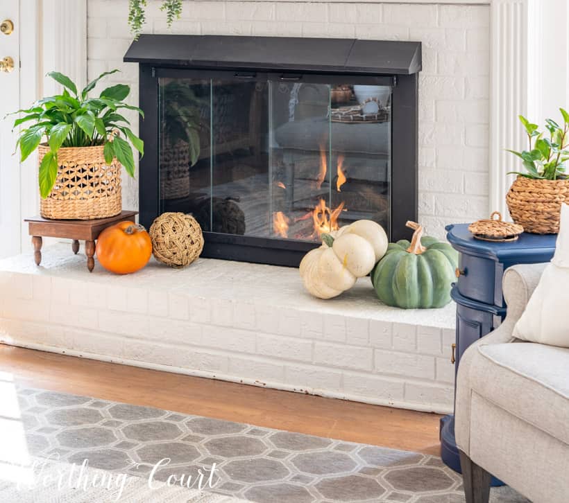 Fireplace hearth decorated for fall with faux pumpkins and an indoor plant.