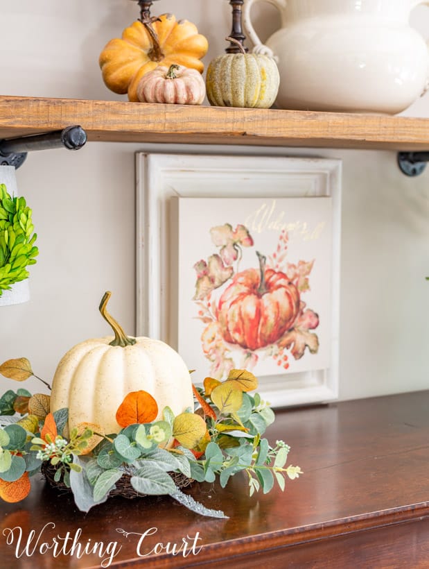 fall vignette with a faux pumpkin nestled in a ring of greenery