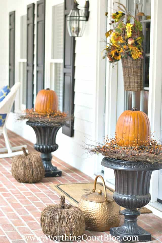 Black urns topped with large pumpkins for fall on the porch.