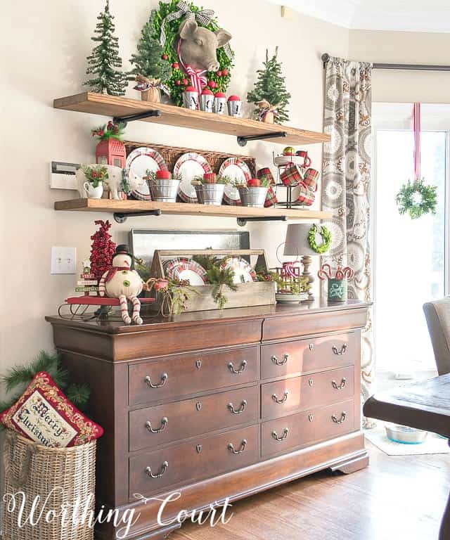 Floating shelves decorated for Christmas with small Christmas trees and a snowman, and Christmas chargers.