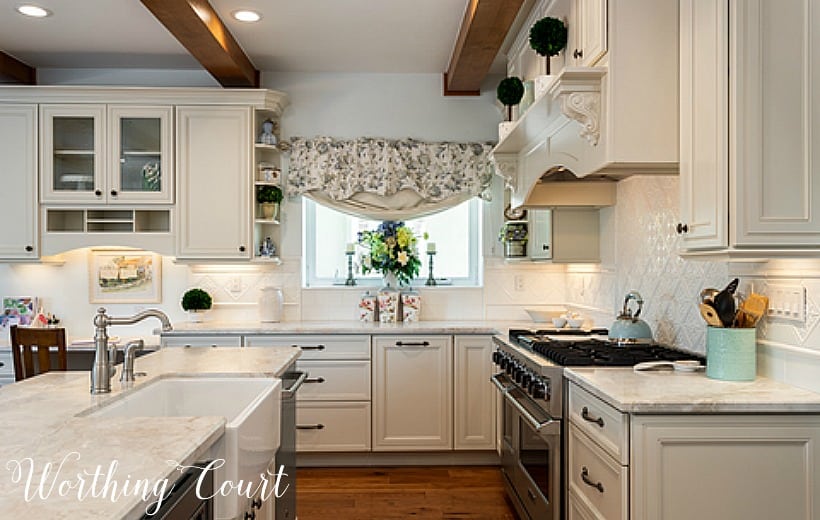 An almost all white kitchen with wooden beams in the ceiling.