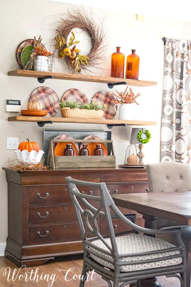 Open floating shelves decorated for fall with amber glass, plaid plates and a fall wreath.