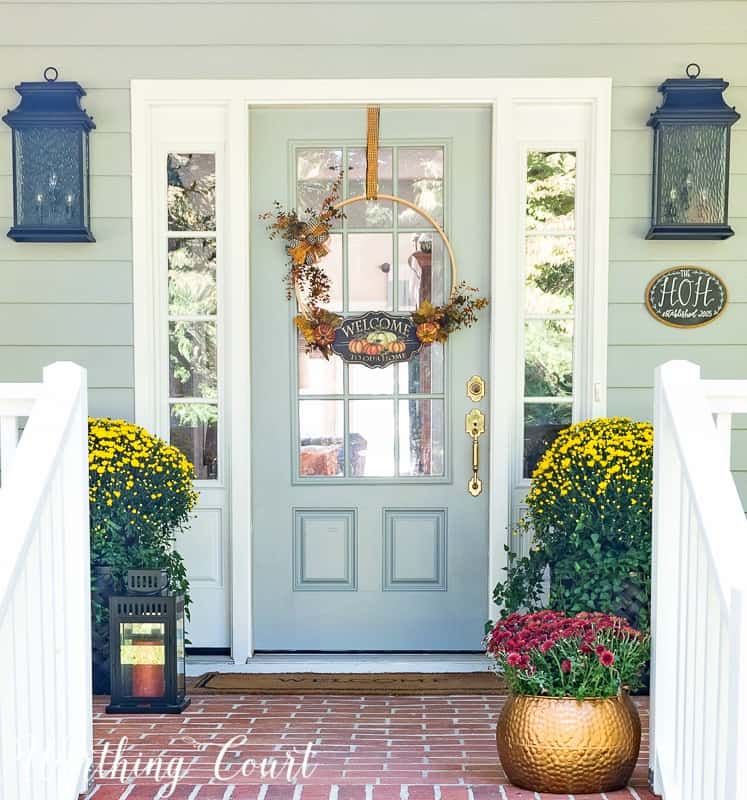 Front porch decorated for fall with mums and a Welcome sign on the door.