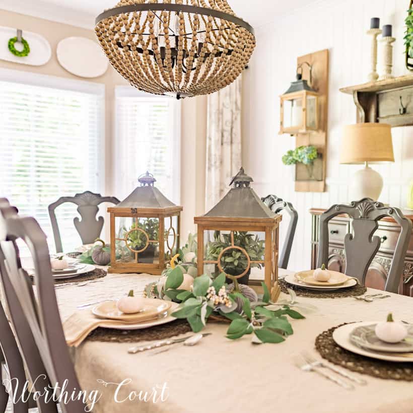 table setting with white tablecloth, white dishes and two lanterns