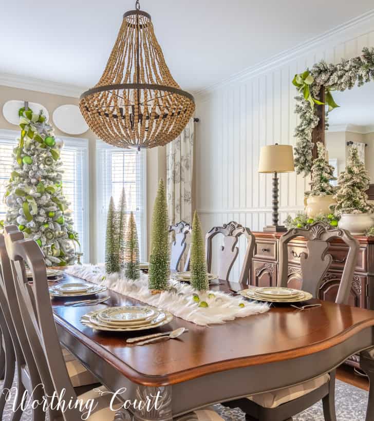 Christmas dining room decor with flocked trees, garland and green and silver ornaments and ribbon.