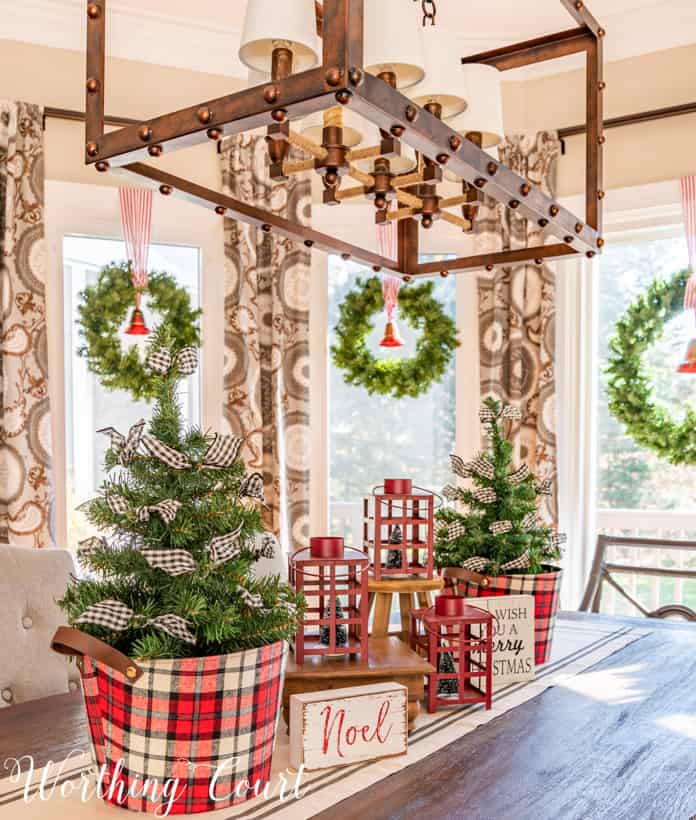 Christmas centerpiece with mini trees in plaid containers and red lanterns.