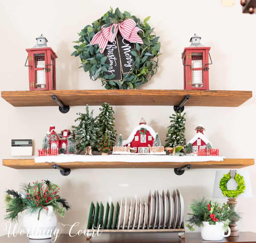 Open shelving unit in the dining room with a Christmas wreath, a little village and Christmas plates.