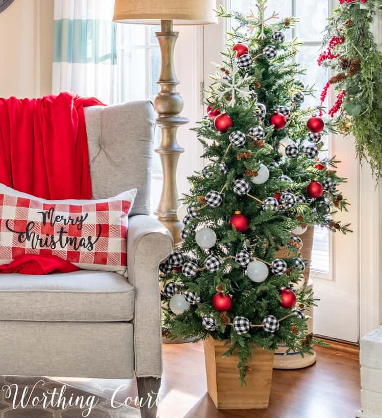 A small pillow that says Merry Christmas is on the armchair beside the tree.