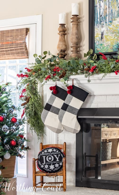 A small wooden chair with a Joy pillow on it is in front of the fireplace.