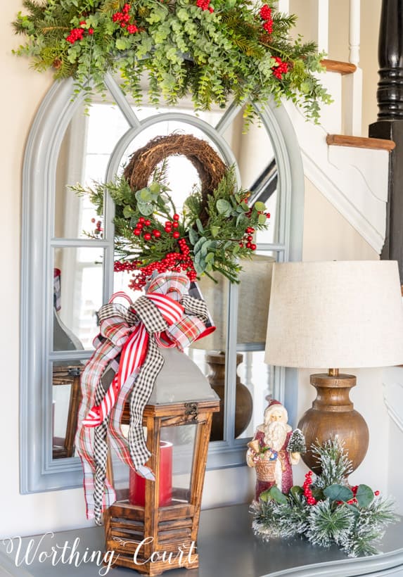 Arched mirror topped with a sway of faux greenery and red berries for Christmas.