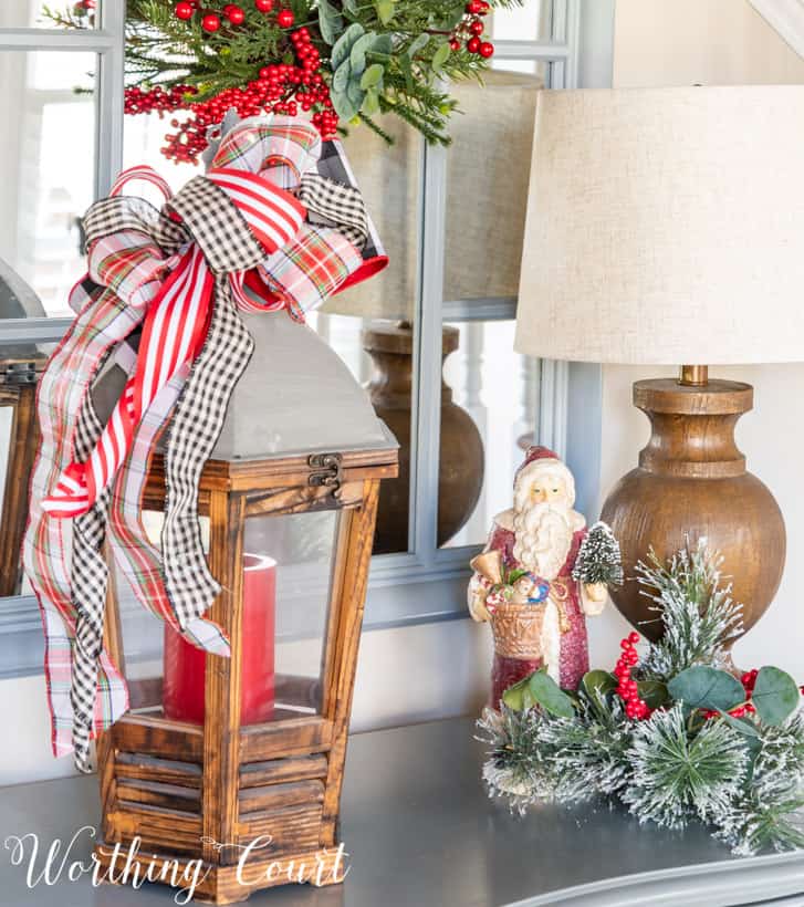 Wood and metal lantern containing a red candle with a bow made from Christmas ribbon attached to the top.