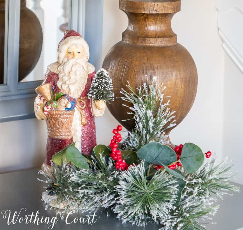 Christmas vignette with Santa figurine and faux greenery at the base of a lamp.