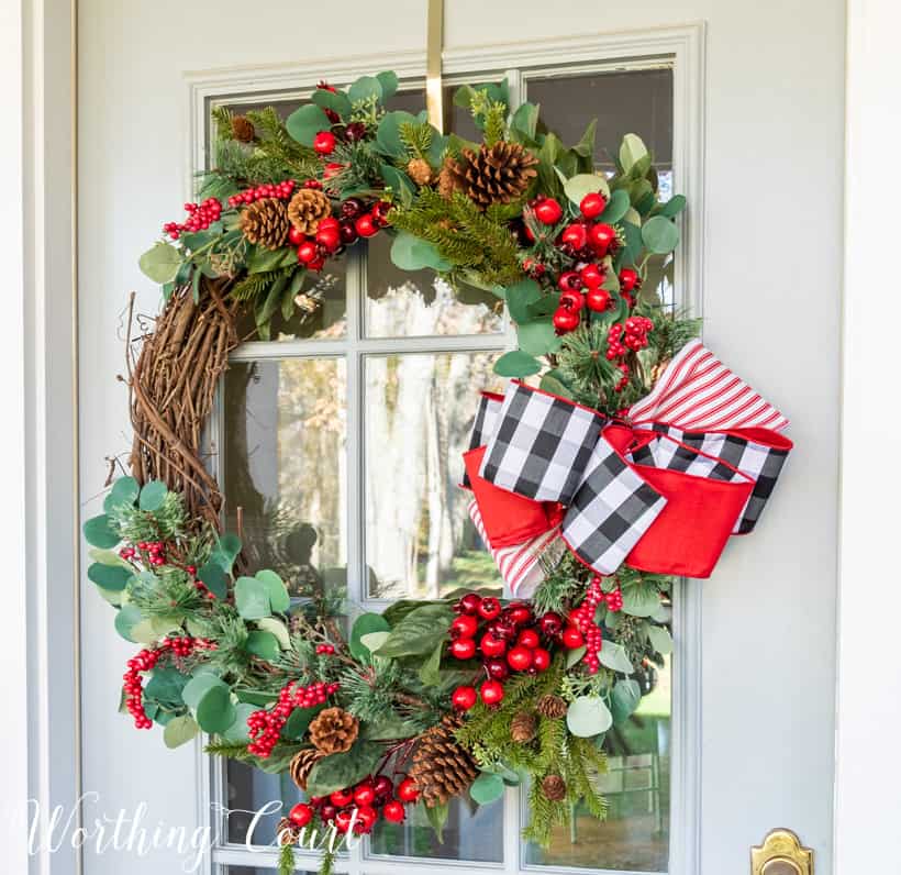 An up close picture of the berry and greenery wreath with a large red, black and white bow on the side.