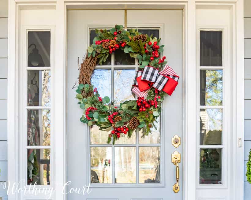 Christmas wreath with black white and red ribbon and greenery and red berry picks.