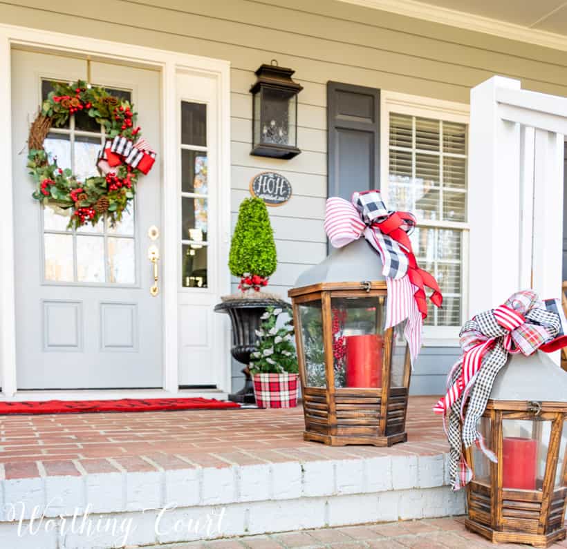 Lanterns with Christmas ribbon and red candles on front porch steps.