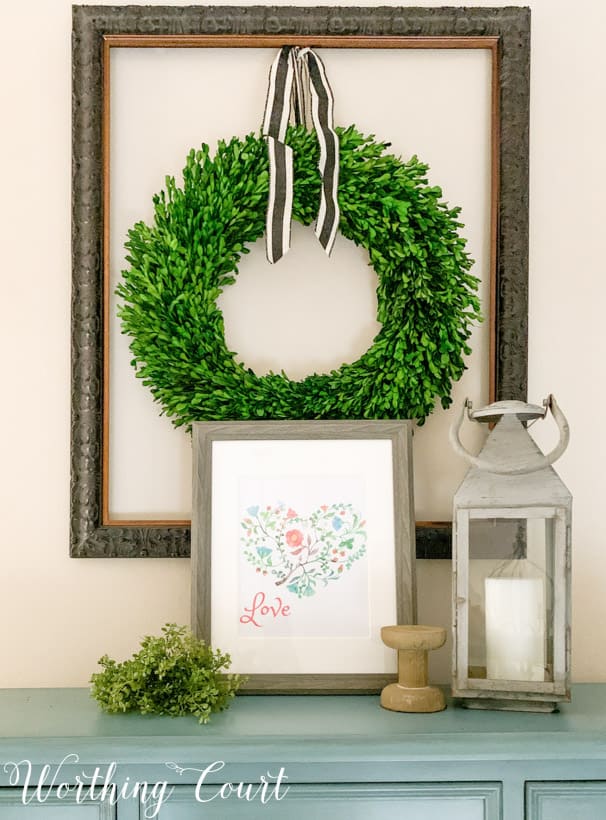 The Valentines printable on a side table with a green wreath on the wall above it.