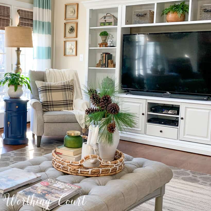 A neutral living room with a small wicker tray and a white vase filled with pine cones on the tray.