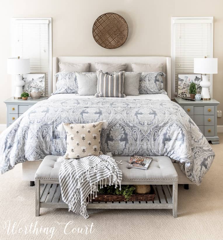 Neutral master bedroom bedding and furniture and a basket on the wall as decor.