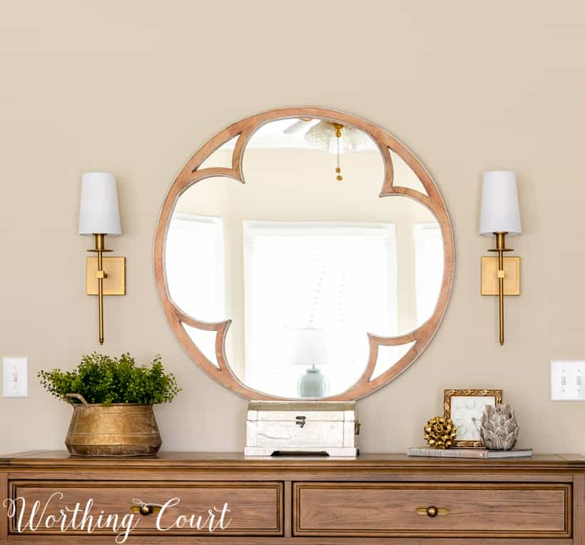 round mirror above dresser flanked by brass sconces