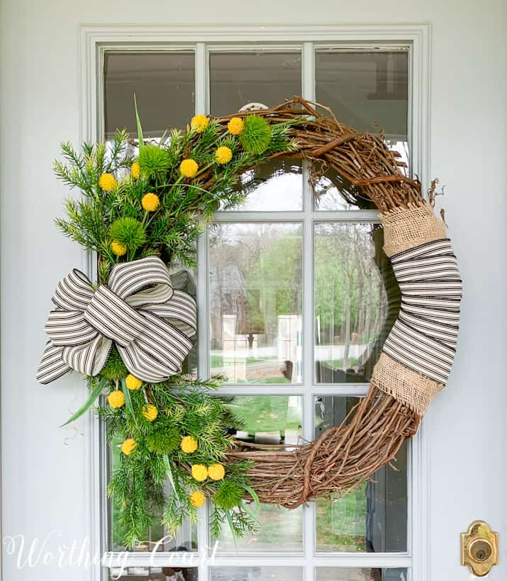 The grapevine wreath with yellow flowers and a black and white bow.