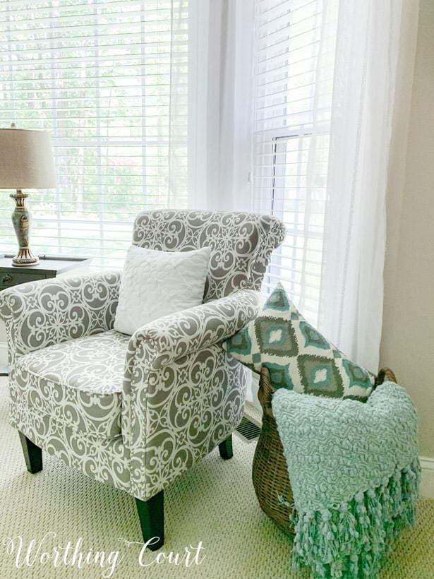 Gray and white arm chair with a large basket beside it filled with blankets and pillows.