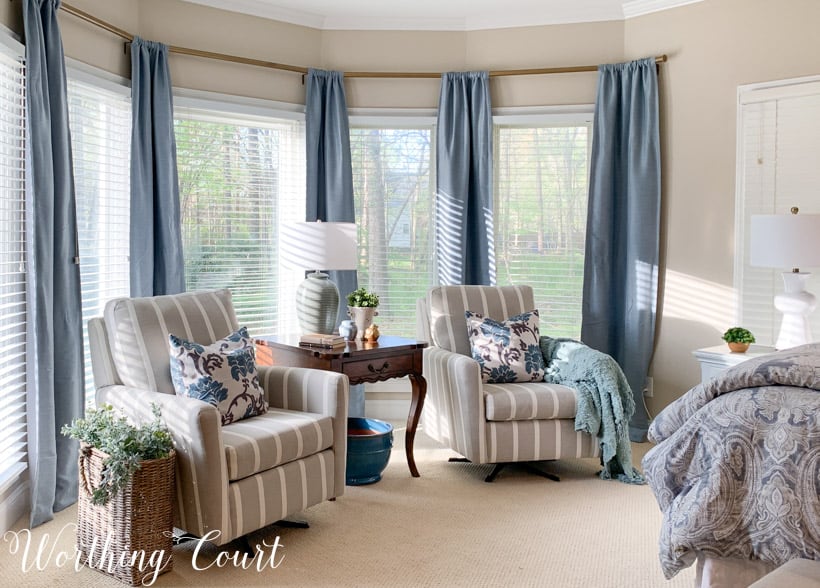 Bedroom bay window sitting area with chairs and blue draperies.