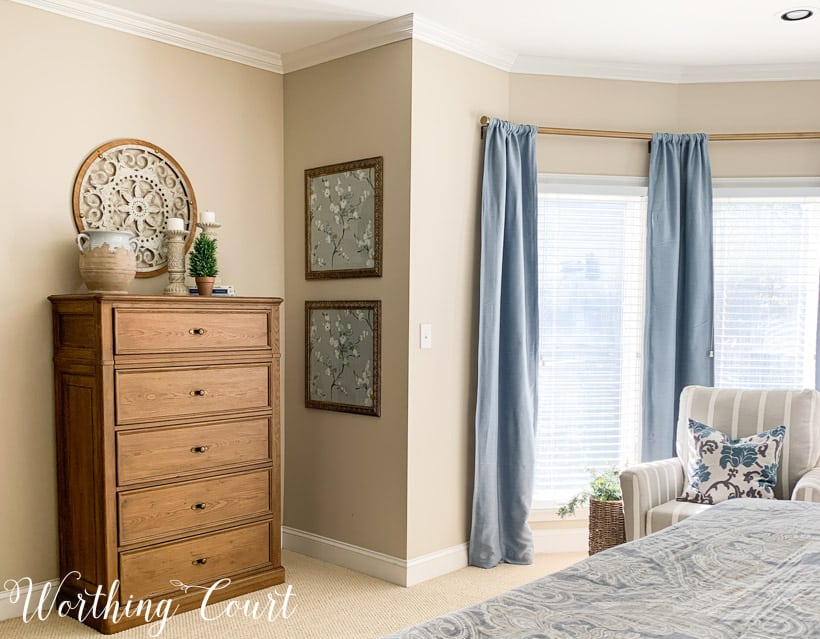 Master bedroom chest of drawers with blue draperies and framed wallpaper.