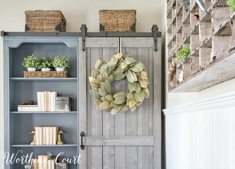 Gray bookcase with sliding door and green leaf wreath on the door.