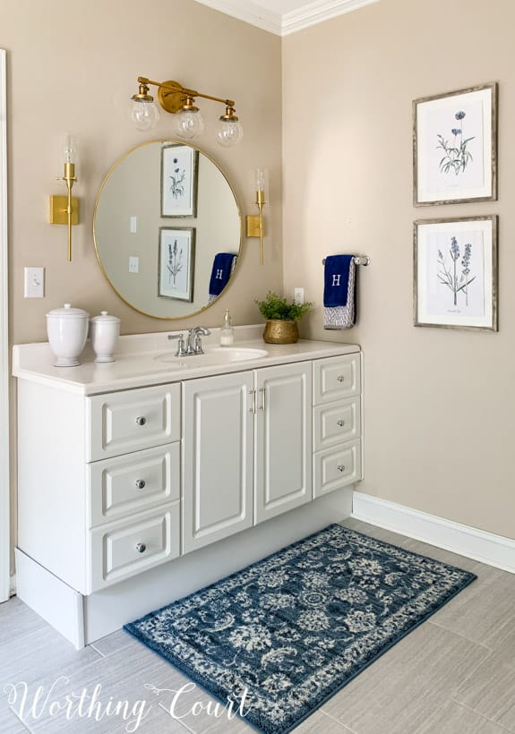 White bathroom vanity with round mirror, gold lights and accessories.