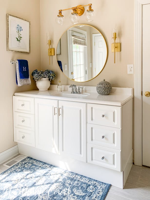 white bathroom vanity with round mirror, gold lights and accessories