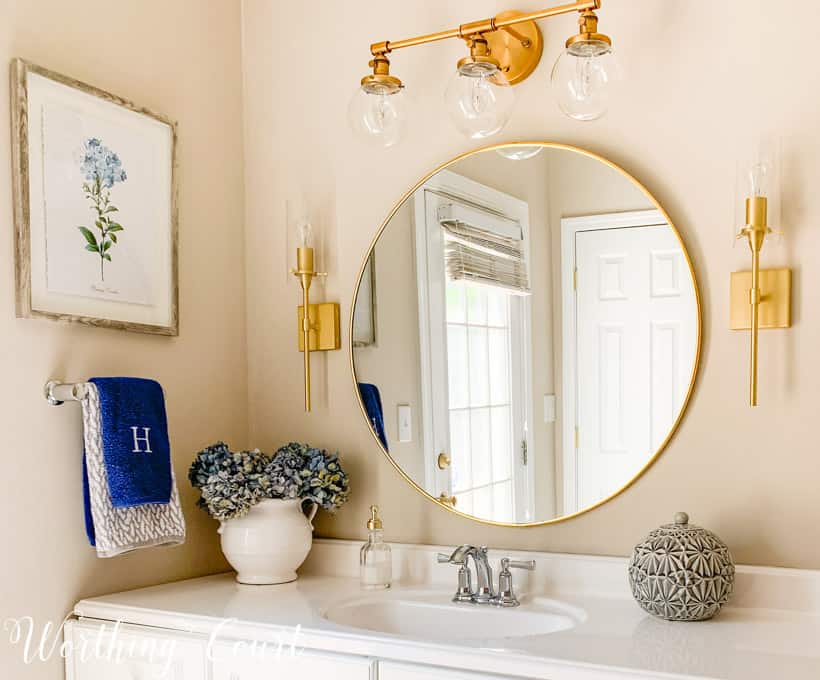 A round gold mirror is above the bathroom sink.